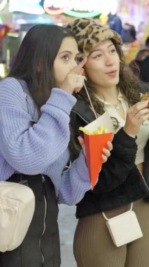 Valencia Lunaparkı 'nda sokak yemeği yiyen iki yetişkin kız ve arka planda insanlar var.