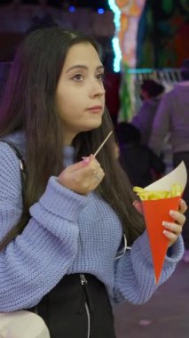 Geceleri Valencia 'da yemek kamyonundan patates kızartması ve waffle yiyen iki kız maskeli insanlar geçerken FullHD dikey video