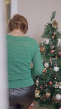 İspanyol kadın dekoratif Bauble 'ı kutusundan alıp evdeki Noel ağacına asıyor. orta çekim - Dikey FullHD video