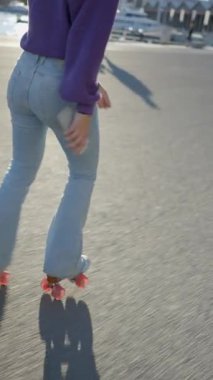 Kotlu kız gün ışığında limanda paten kayıyor, arkadan görünüyor - FullHD dikey video