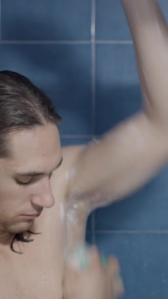 若い慎重な長髪の男は 彼の脇の下をこすり シャワーで彼の腕 クローズアップショット 垂直ビデオ — ストック動画