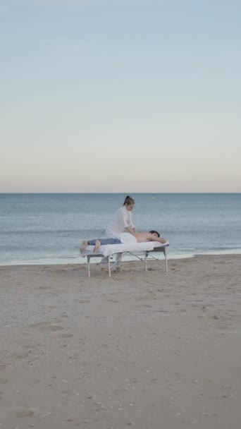 海岸でクライアントに癒しの治療を与えるプロのマッサージセラピストのワイドショット フルHd垂直ビデオ — ストック動画