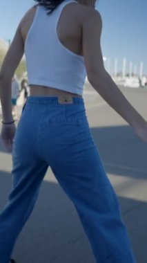 Koyu renk saçlı kız güneşli marinadaki teknelerle paten kayarak dolanıyor.