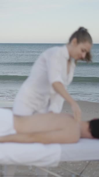 バックグラウンドの海の波 および前景に焦点を当てていないマッサージを行っている女性 フルHd垂直ビデオ — ストック動画