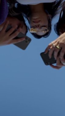 Genç, mutlu, koyu renk saçlı kadınlar, FullHD dikey video kasetinden görülebilen telefonlar ve sohbetler kullanıyorlar.