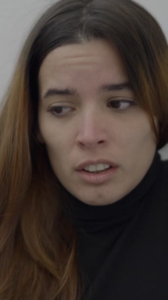 恐ろしい表情で壁に座っている若い女性のクローズアップ 1080 垂直ビデオ — ストック動画