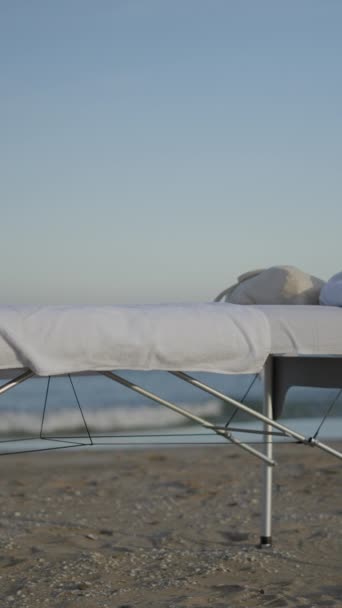 ビーチでのマッサージテーブル 背景にある海の波 雲はない フルHd垂直ビデオ — ストック動画