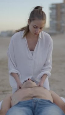 Genç erkek plajda masaj yapmaktan hoşlanır. Sağlık ve vücut bakımı konsepti - ön görüş - FullHD dikey video