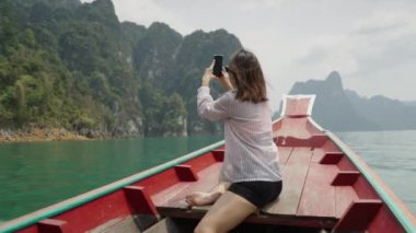 Tahta bir teknede bir kadın gölün fotoğraflarını çekiyor - 4K yatay görüntü.