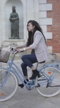 Parkta bisiklet süren uzun siyah kıvırcık saçlı Faslı kadın. iz çekimi - Dikey