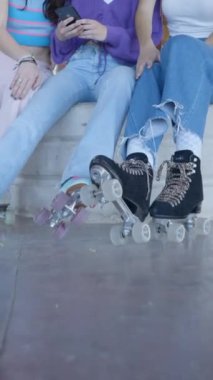 Patenli üç kız oturur ve telefona bakar ve güler, eğilir - FullHD dikey video