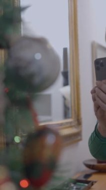 Yaşlı İspanyol kadın evde akıllı telefon kamerasıyla Noel ağacı dekoru çekiyor. orta çekim - Dikey FullHD video