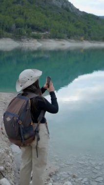 Şapkalı ve arkası olan kız, arkadan görülmüş, telefonlu göl filmi - dikey video