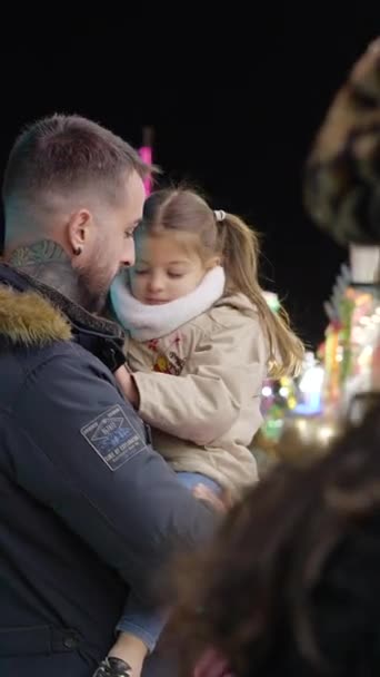 在瓦伦西亚游乐场 年轻父亲与一个小女孩聊天 晚上抱着她的胳膊 背景上闪烁着吸引人的光芒 Fullhd Vertical视频 — 图库视频影像