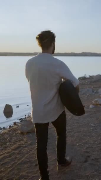 Widok Tyłu Hipstera Spacerującego Wzdłuż Plaży Przed Słońcem Trzymającego Gitarę — Wideo stockowe