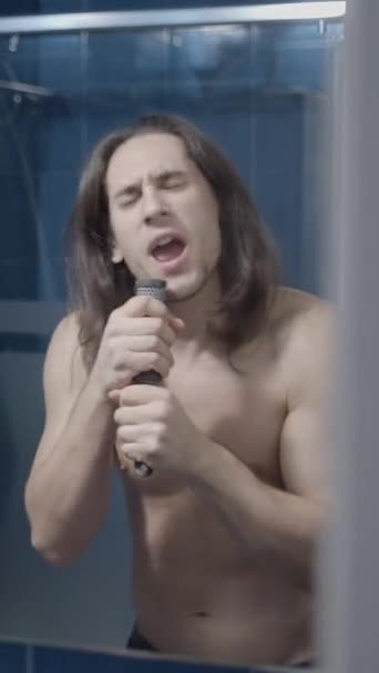 Langhaariger Mann Singt Vor Einem Badezimmerspiegel Mit Einer Haarbürste Als — Stockvideo