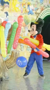 Valencia Eğlence Fuarı - Mickey Mouse kostümlü adam çocuklar gece trende hız trenine binerken şişirilmiş balonları dağıtıyor - FullHD dikey video