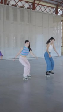 Üç kız paten kayarken ayaklarını tutuyor, ileri doğru kayıyor, çekimleri takip ediyor - FullHD dikey video