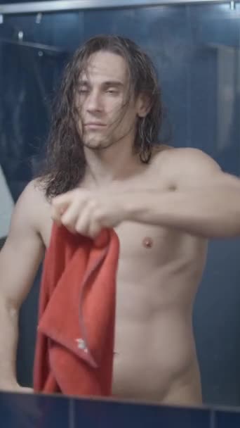 赤いタオルでシャワーを浴びた後 バスルームミラーの前に髪を乾かす若い男 ミドルショット 垂直ビデオ — ストック動画