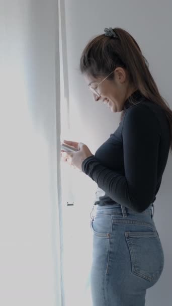 哥伦比亚一所大学的一名年轻学生休学了 小女孩站在窗前用她的电话 1080个垂直录像 — 图库视频影像
