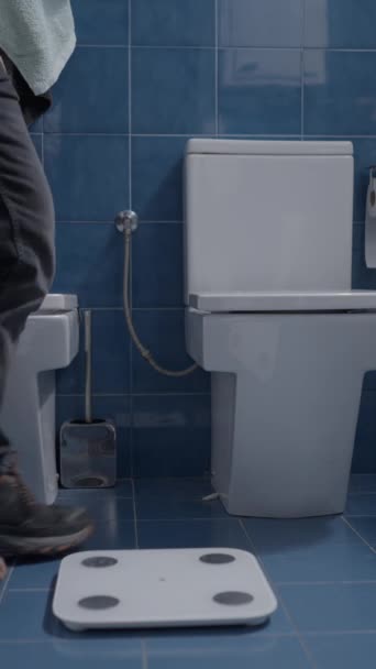 男人在没有鞋子的浴室里称自己的重量 垂直录像 — 图库视频影像