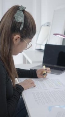 Çalışma masasında oturan ve çalışma malzemelerini vurgulayan genç bir kız. Kolombiya Üniversitesi 'nde okuyan bir öğrenci. - 1080 dikey video