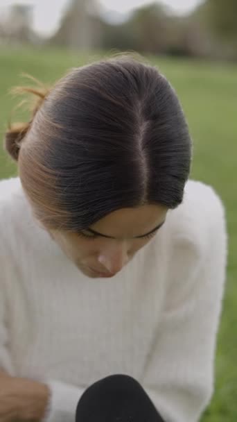 Zamartwiona Młoda Kobieta Siedzi Trawie Drapie Się Ramieniu Patrzy Dół — Wideo stockowe
