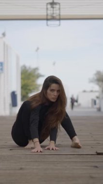 Genç kadın ahşap köprüde oturuyor ve kameraya doğru emeklemeye başlıyor - 1080 dikey video