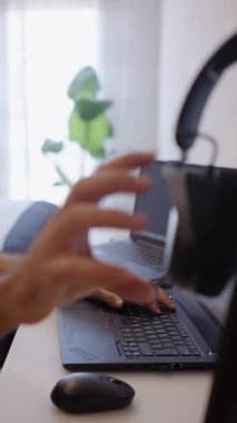 Güney Amerikalı adam bilgisayarı FHD dikey video üzerinde çalışırken kulaklıklarını kaldırıyor.