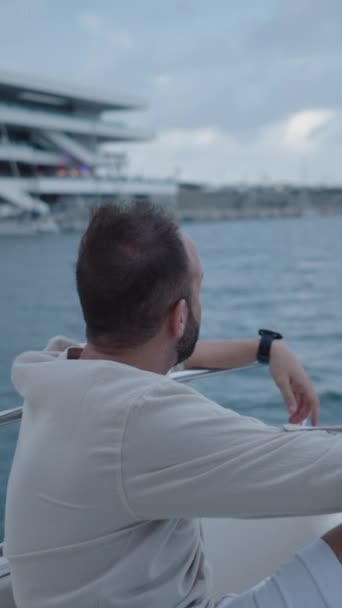 バレンシア港を背景にボートに座っているひげを持つ少年 垂直Fhdラグジュアリーライフスタイル — ストック動画