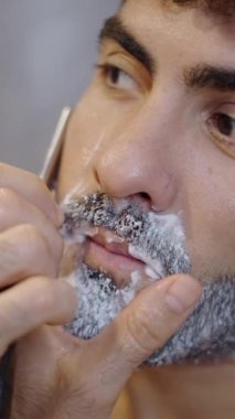 Evde jiletle tıraş olan yakışıklı bir adam - FHD dikey video