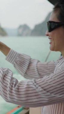 Gömlek ve gözlük takan bir kadın bir gölün fotoğrafını çekiyor - Dikey 1080 Video