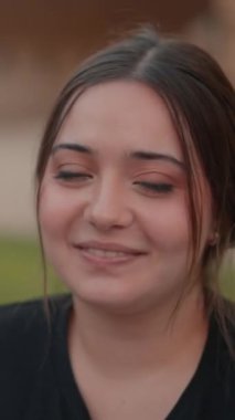 Kahverengi saçlı, el sallayan ve utanarak gülen çekici genç bir kadın. Kapat - Dikey 1080 video