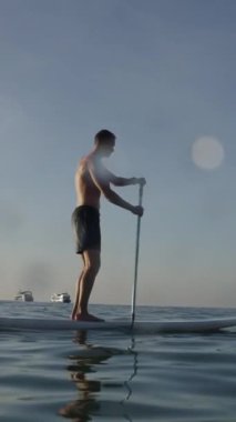 Batılı adam denizde sörf tahtası üzerinde kürek çekiyor - FHD Dikey