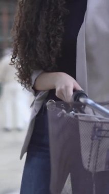 Uzun ve kıvırcık saçlı güzel bir kadın bisiklet ile cadde boyunca yürüyor. Yakın plan, Yan Görünüm - Dikey