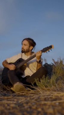 Mavi gökyüzüne karşı gitar çalan dalgın sakallı hippi, dikey FullHD videosu.