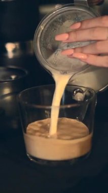 Ofisteki kahve dükkanında bir fincan sade kahveye taze süt döken kadın elleri. Kapat - Dikey