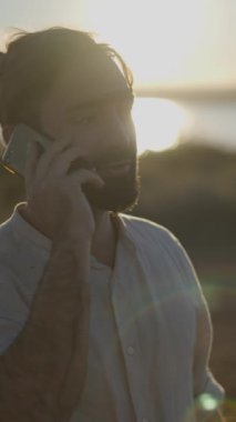 Günbatımı ışıklarıyla cep telefonuyla konuşan genç adam - Dikey FullHD video