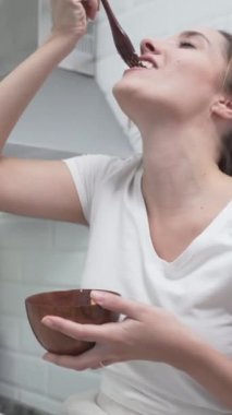 Neşeli Kadın, mutfakta yemek yerken ahşap çatalını mikrofon olarak kullanıp şarkı söylüyor. Yakın plan - Dikey