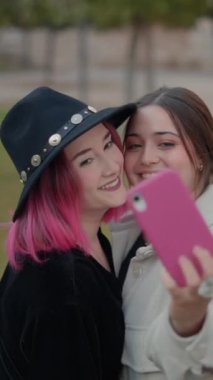 Güzel makyaj arkadaşları parkta akıllı telefonlarıyla selfie çekiyorlar. 1080 dikey video.