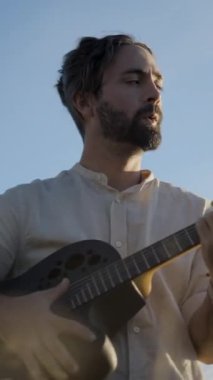 İspanyol sakallı maço gitarist akustik gitarist ve mavi gökyüzü arka planına karşı aşk şarkısı söylüyor.