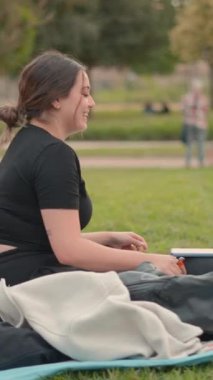 Şehir parkında çimlerin üzerinde oturan ve eğlenen iki arkadaşın videosu dikey 1080.
