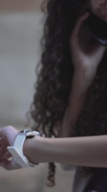 Akıllı telefondan konuşan kız kol saatine bakıyor. Kapat - Dikey