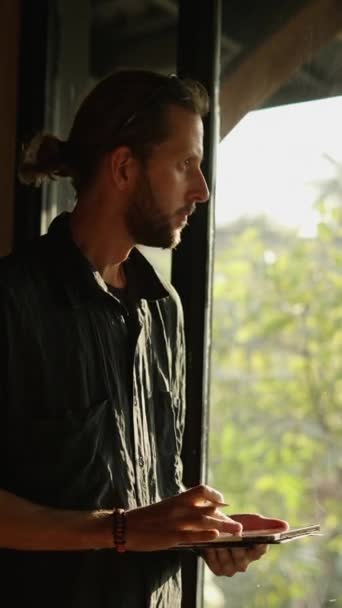 一个留着大胡子的瘦长男子手里拿着平板电脑望着窗户 Fhd垂直录像 — 图库视频影像