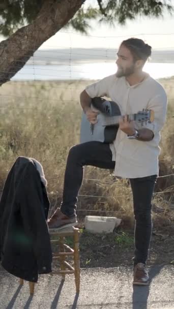 スペイン語のマチョ男は アコースティックギタースタンディングロードサイドで歌い スペインの田舎の日没でカメラを見て歌う スローモーションをパンニング 垂直フルHdビデオ — ストック動画