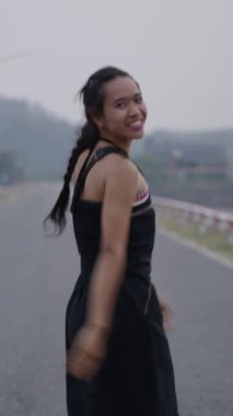 Bir yolda Asyalı bir kadın zıplıyor ve gülümsüyor - 4K Yatay yaşam tarzı videosu