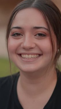 Kahverengi saçlı, yüzünde mutluluk ifadesi olan, gülen, dikey 1080 videolu pozitif kızın yakın çekimi.
