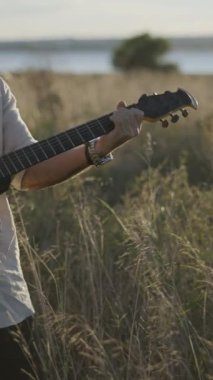 İspanyol gitarist sonbaharda çayırlarda akor çalıp Torrevieja Pembe Gölü yakınlarındaki siyah akustik gitarda şarkı söylüyor - Dikey FullHD video