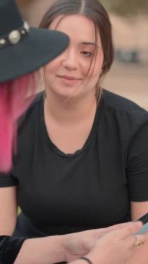 Kahverengi saçlı genç kadın arkadaşıyla konuşurken her ikisi de cep telefonu ekranına, yavaş çekim sahnesine, dikey 1080 video görüntülerine bakıyor.