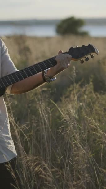 去年秋天 西班牙吉他手在草坪上演奏和弦 并在Torrevieja Pink Lake附近的黑声吉它上唱歌 垂直Fullhd视频 — 图库视频影像